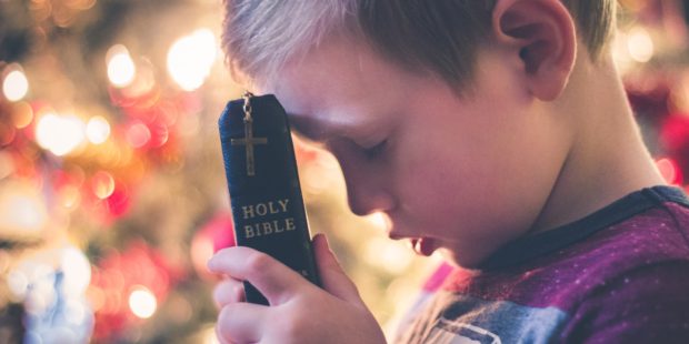 Betender Junge hält eine Bibel in der Hand.