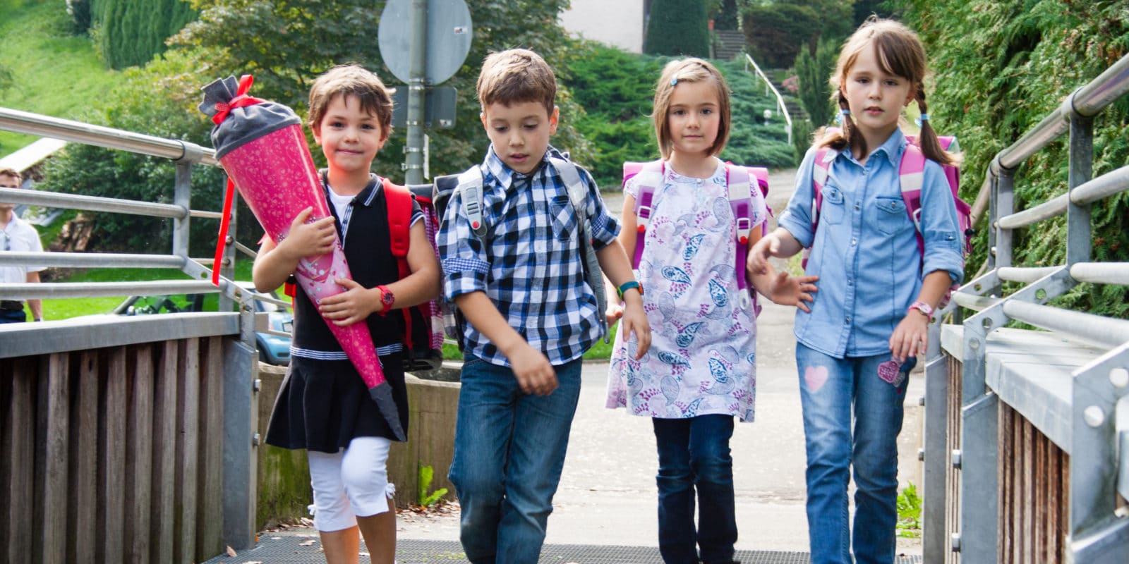 vier Schulkinder gehen in einer Reihe über eine Brücke