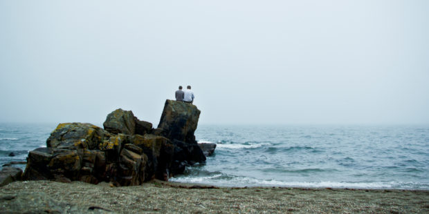 zwei Mensche sitzen auf Fels am Meer