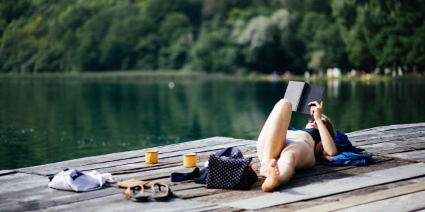 Frau im Bikini liegt auf einem Steg und liest ein Buch