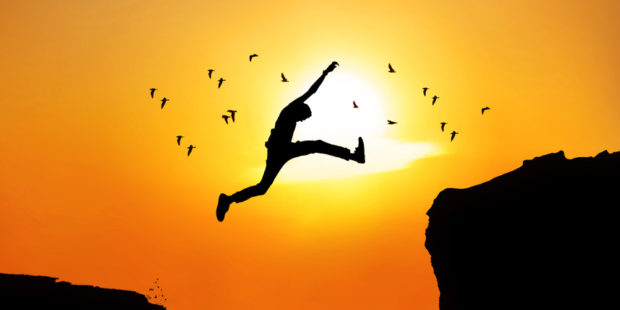 Ein Mann springt über eine Schlucht, im Hintrergrund die Sonne und Vögel