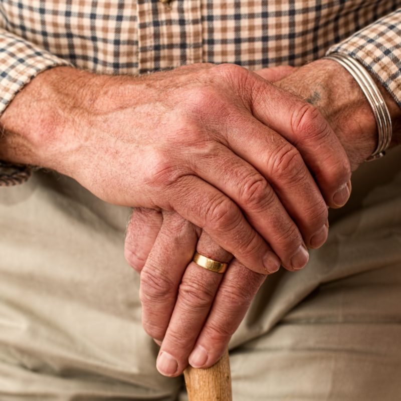 Hände eines alten Mannes lehnen auf einem Stock