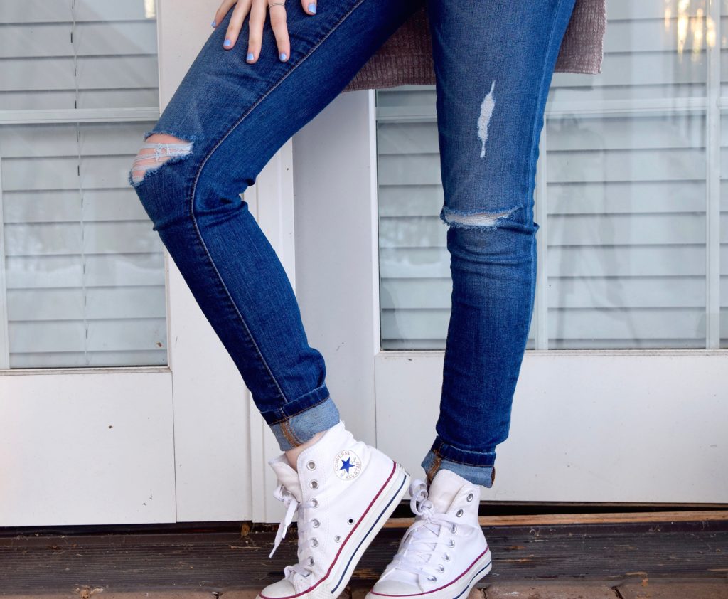 Beine in zerissenen Jeans und Turnshuhen
