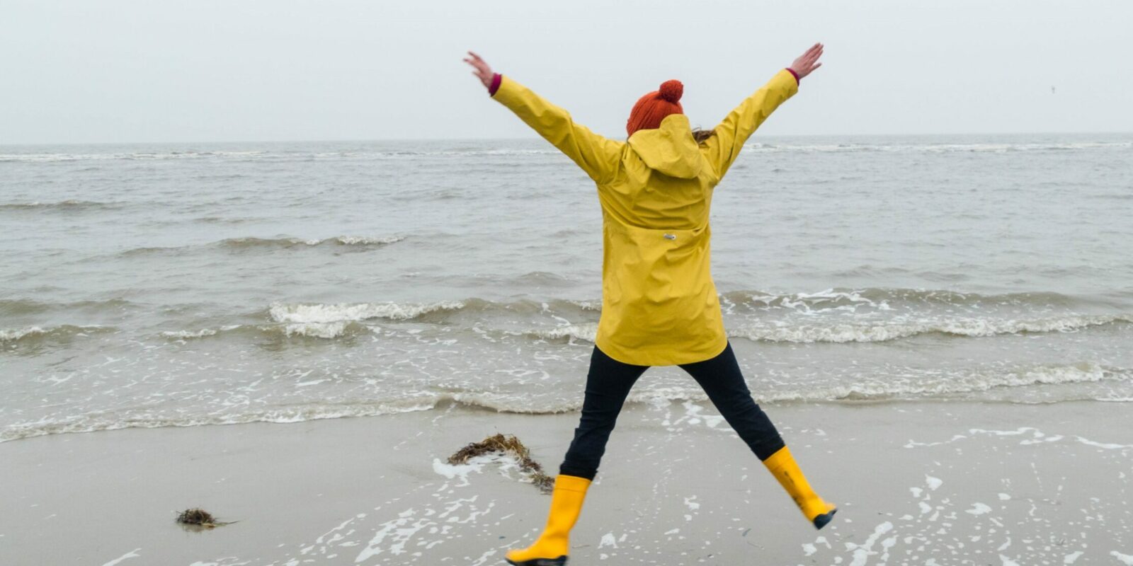 Frau im Regenmantel macht Freudensprung