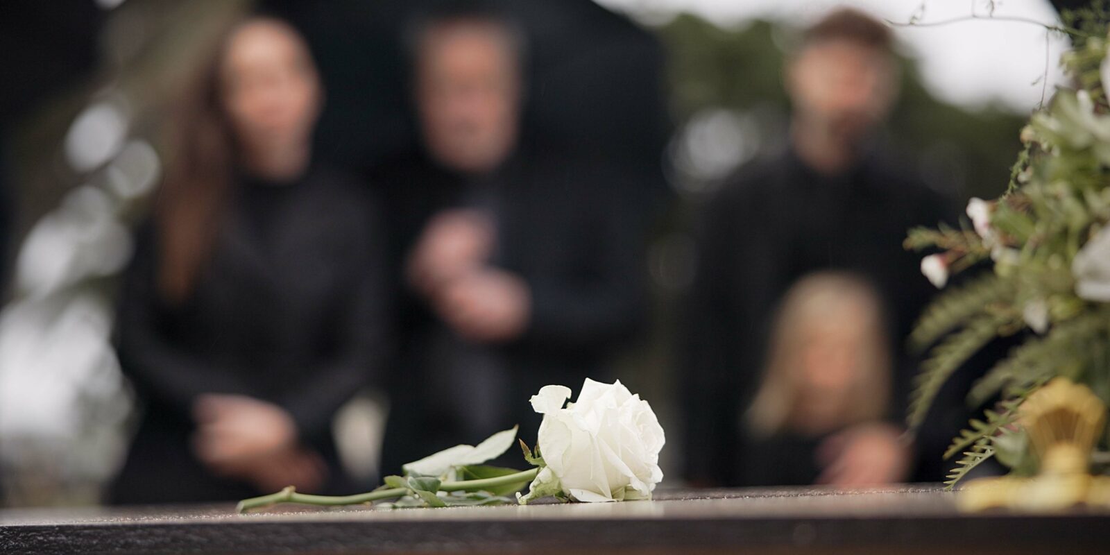 Eine Rose auf einem Sarg mit Menschen im Hintergrund