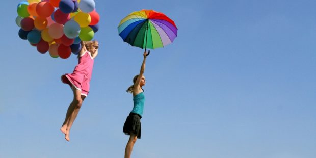 Zwei Mädchen fliegen mit bunten Ballons und einem Regenschirm durch die Luft.