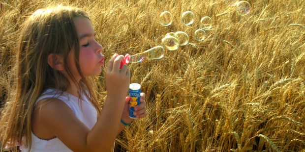 Mädchen macht Seifenblasen in einem Kornfeld