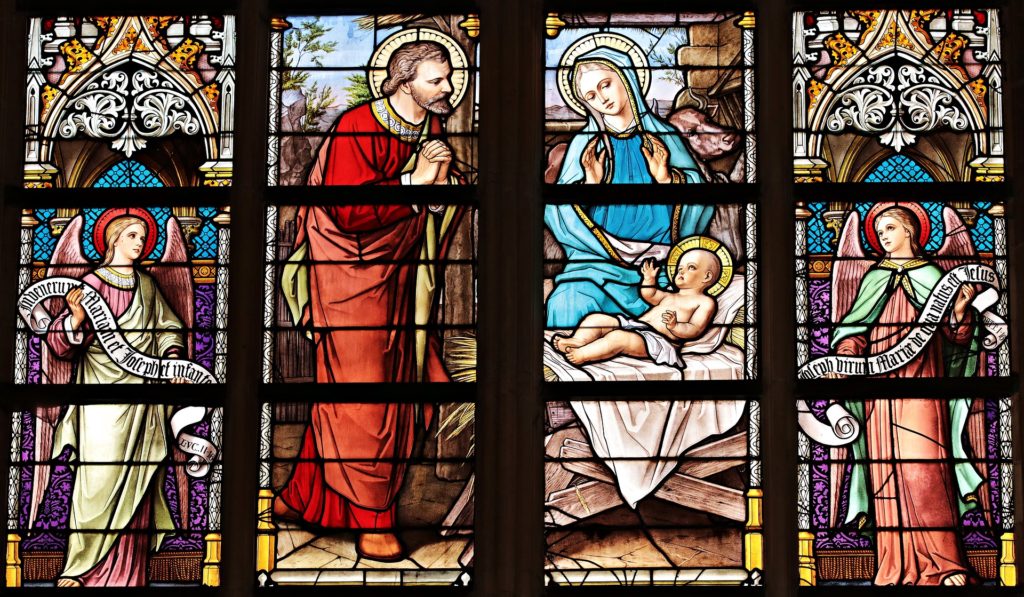 Ein Kirchenfenster, auf dem Engel, Maria, Josef und das Jesuskind abgebildet sind.