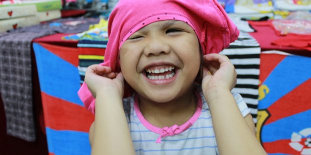 Ein kleines Mädchen will sich ein Shirt falsch herum auf den Kopf ziehen.