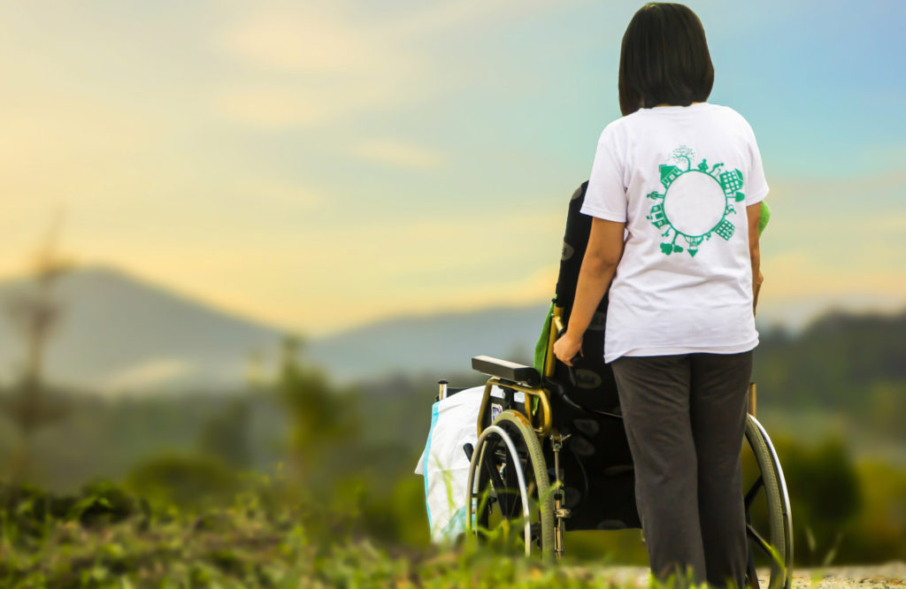 Eine Frau steht mit einem Rollstuhl in einer Naturlandschaft