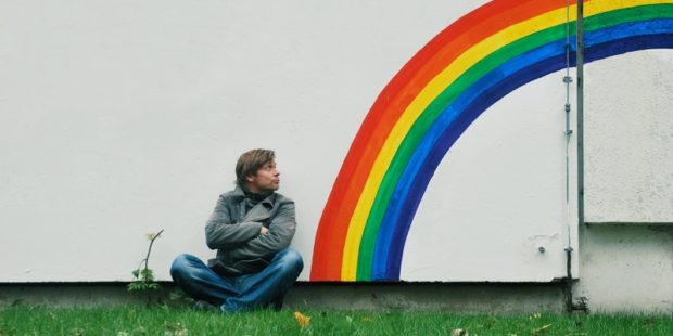 Mann sitzt neben Regenbogen