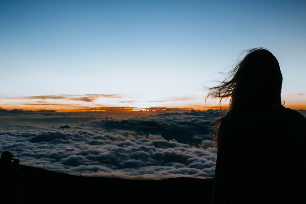 Eine Frau überblickt den Sonnenaufgang über den Wolken.
