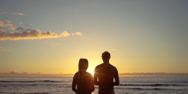 Paar blickt über das Mehr in den Sonnenaufgang.