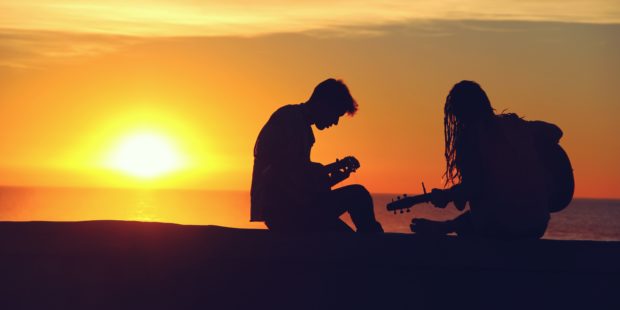 Silhouette eines Pärchens, das im Sonnenuntergang Gitarre spielt.