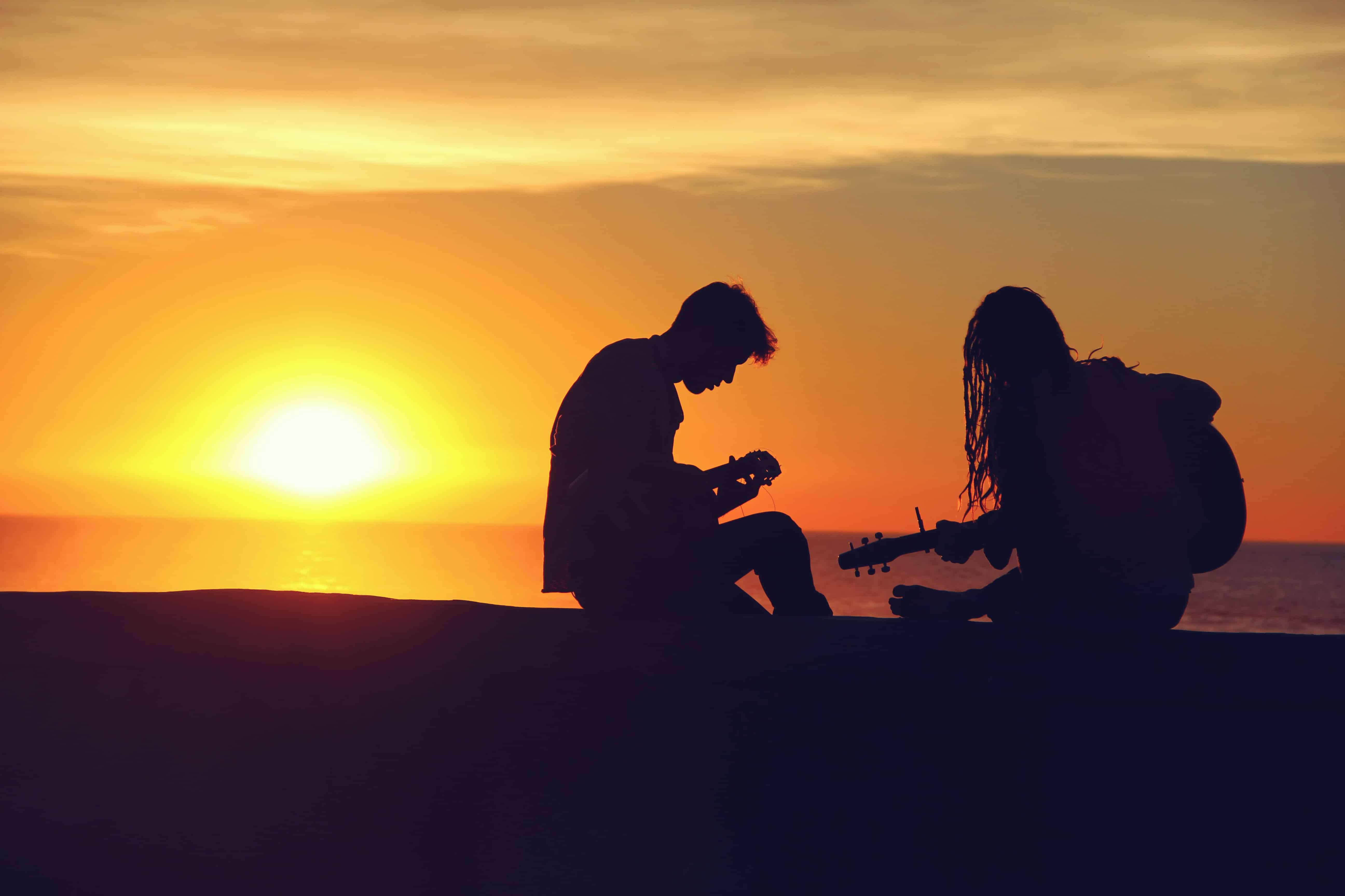 Silhouette eines Pärchens, das im Sonnenuntergang Gitarre spielt.