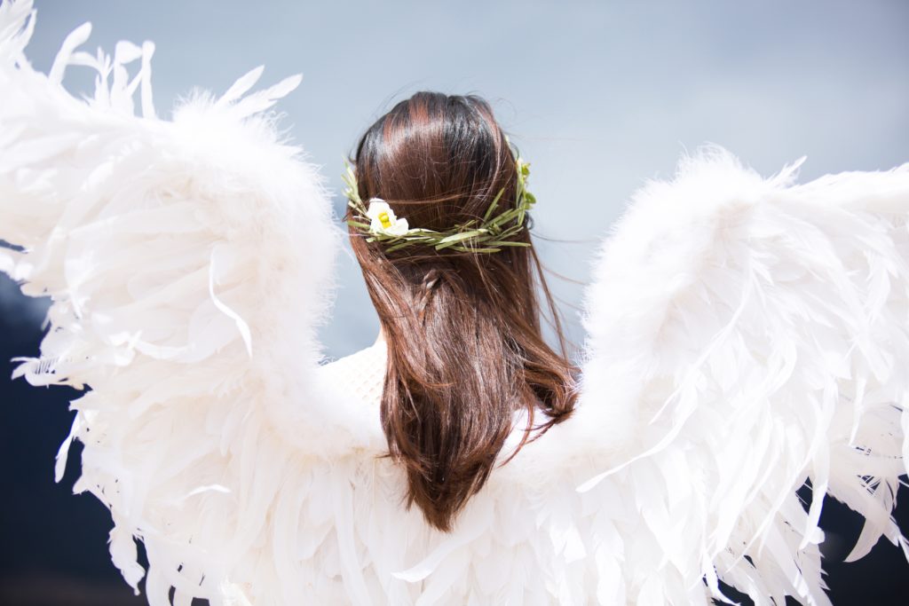 Frau mit Engelsflügeln und Blumenkranz im Haar.