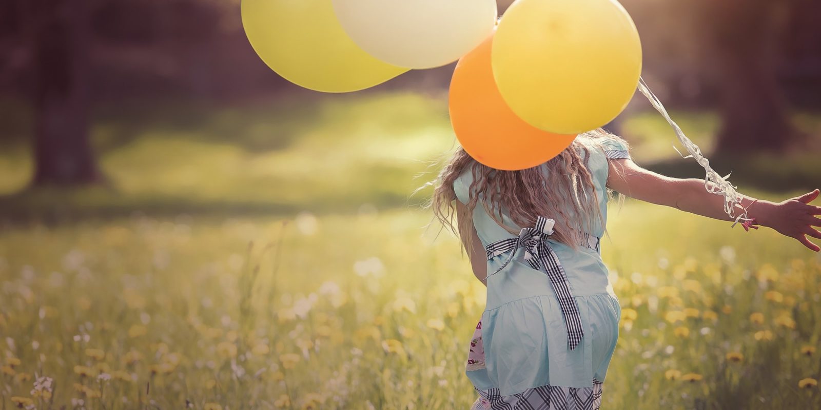 Mädchen mit Luftballon läuft über Wiese