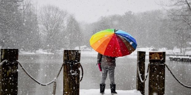 eine Person steht mit buntem Schirm im Schneetreiben