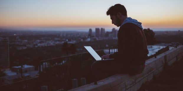 Mann sitzt im Halbdunkel mit Laptop auf einem Dach