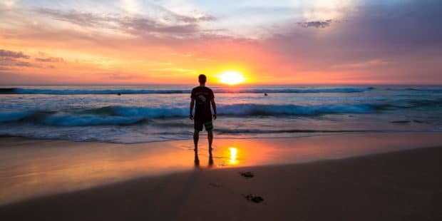 Mann steht bei Sonnenuntergang am Strand