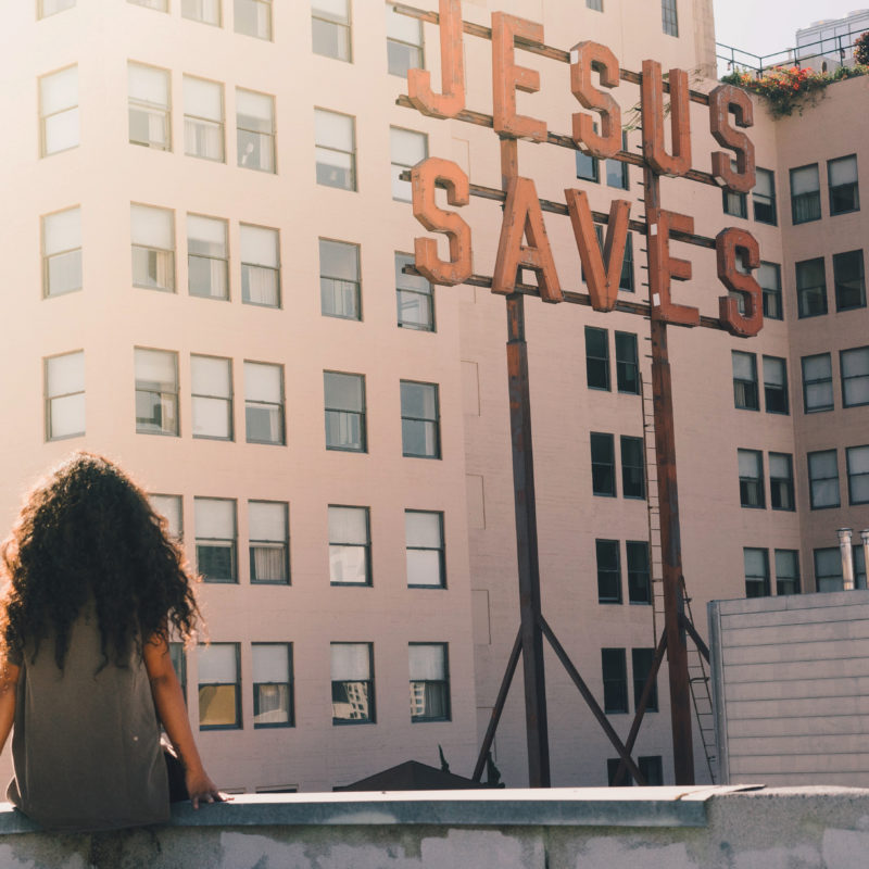 Frau sitzt auf einem Dach und schaut auf Jesus-Schriftzug