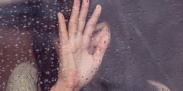Eine traurige Frau an einer Fensterscheibe