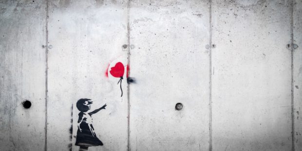 Kind mit roten Luftballon vor grauer Wand
