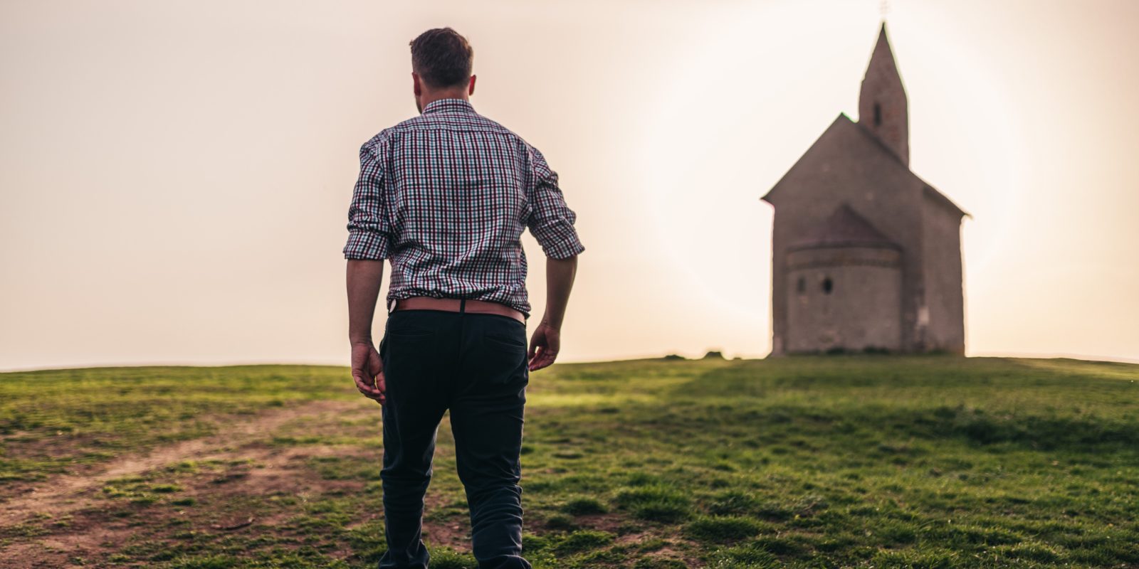 Mann geht über Wiese auf Kirche zu