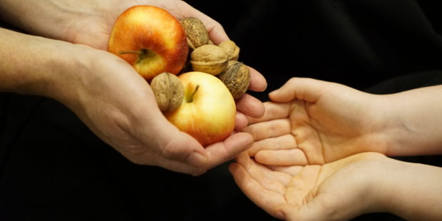 Zwei Händepaare, die eine gibt Äpfel und Nüsse in die andere.
