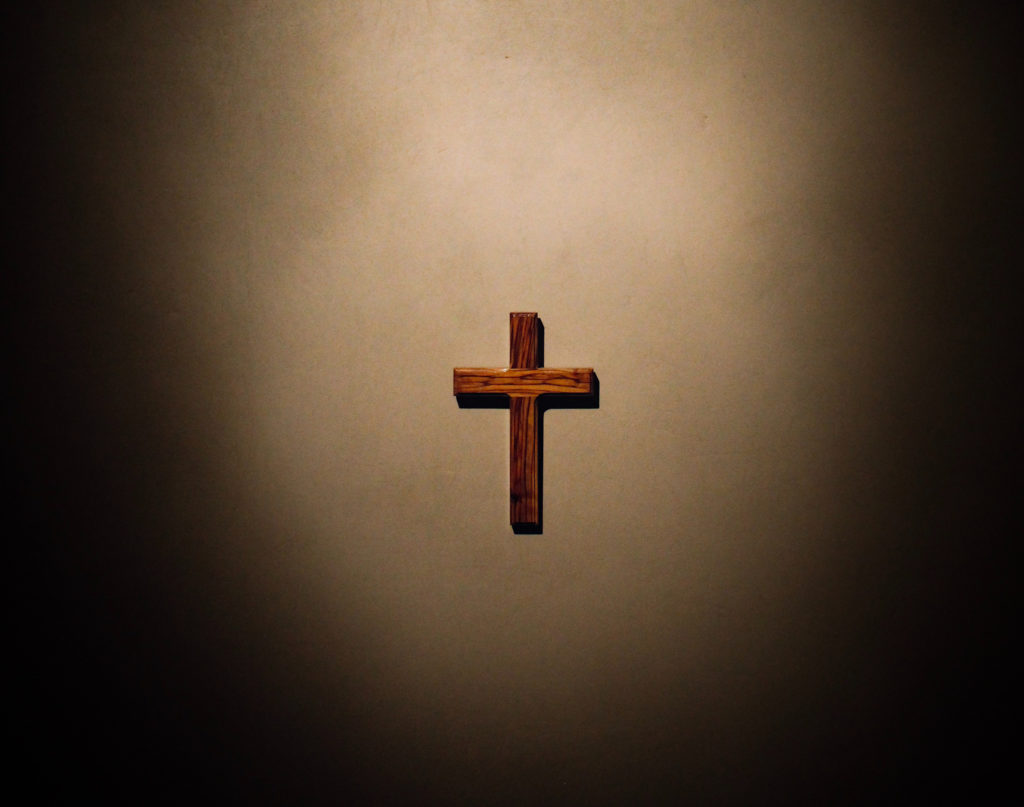 Kreuz hängt im Lichtschein an der Wand