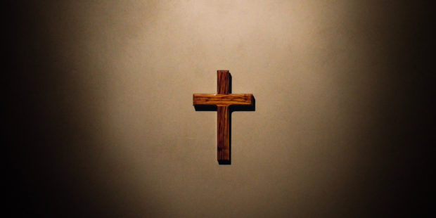 Kreuz hängt im Lichtschein an der Wand