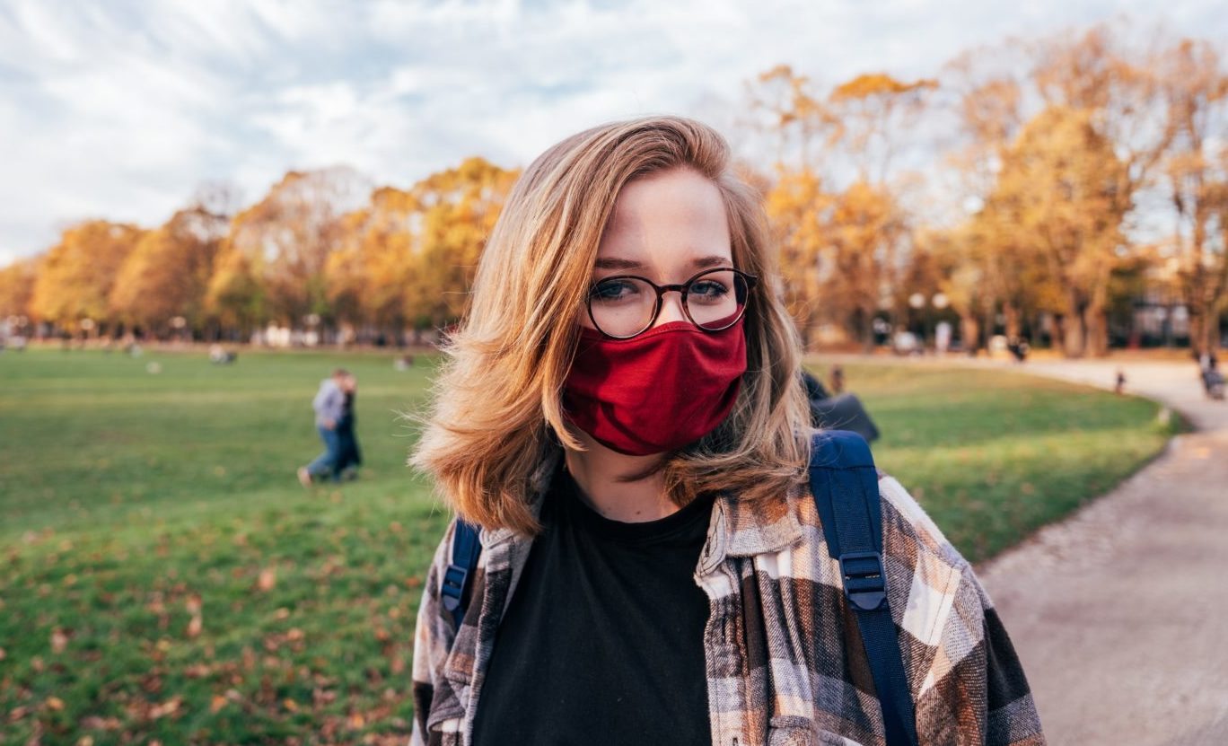 Eine Frau im Jacket mit Brille steht in einem Park