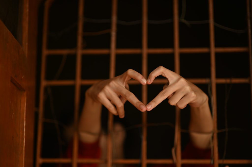 Eine Person hinter Gitterstäben zeigt mit den Fingern ein Herz.