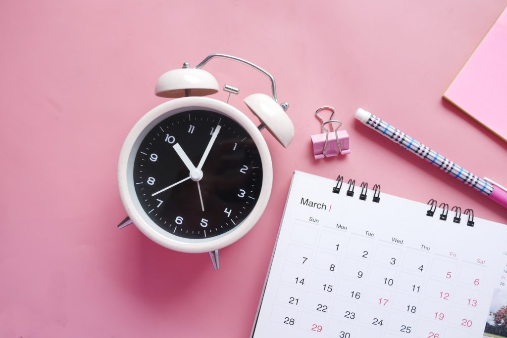 Wecker, Kalender, Schreibuntensilien auf rosafarbenen Hintergrund