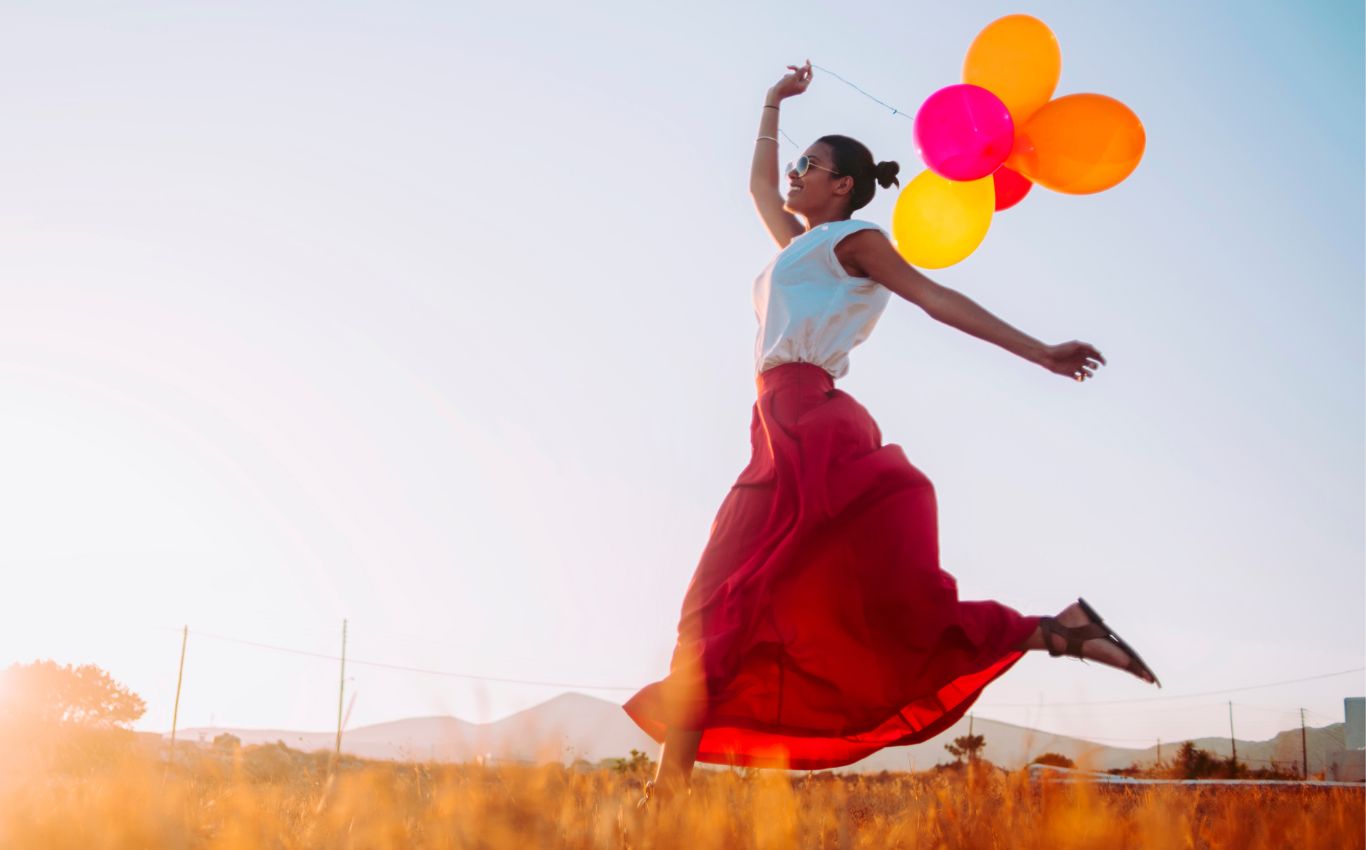 Glückliche Frau mit Ballons, die über ein Feld rennt