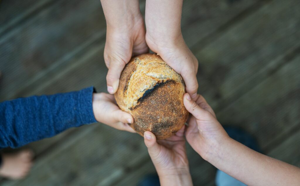 Hände die gemeinsam ein Brot festhalten.