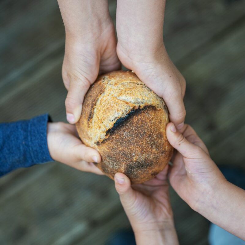 Hände die gemeinsam ein Brot festhalten.