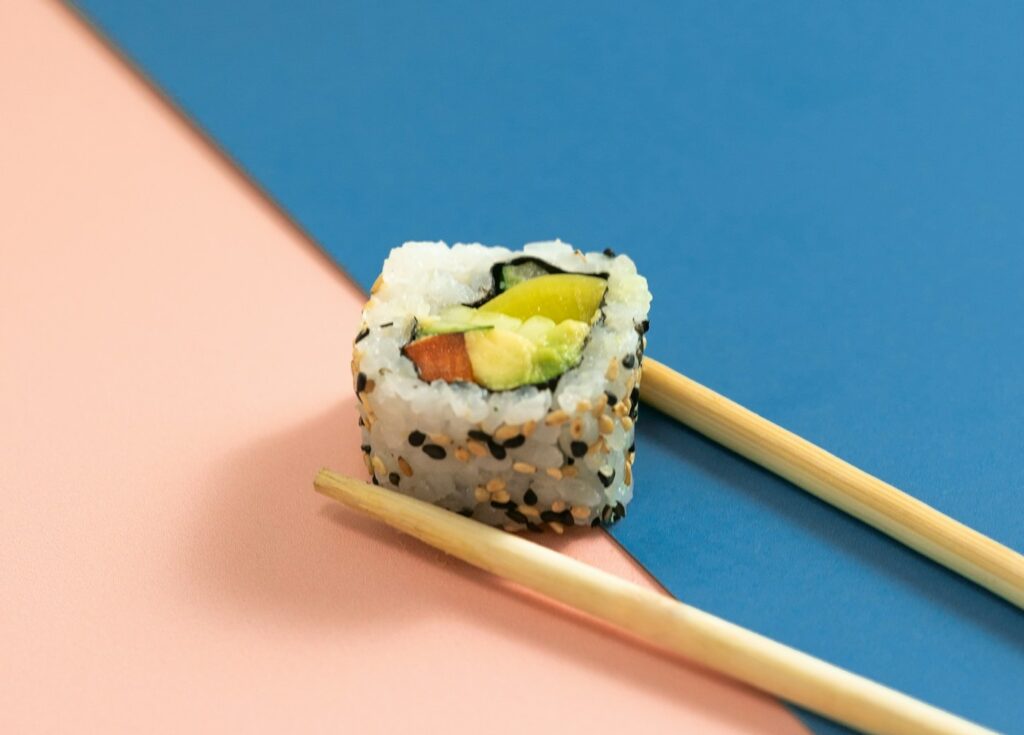 two chopsticks with sushi on them on a blue and pink background