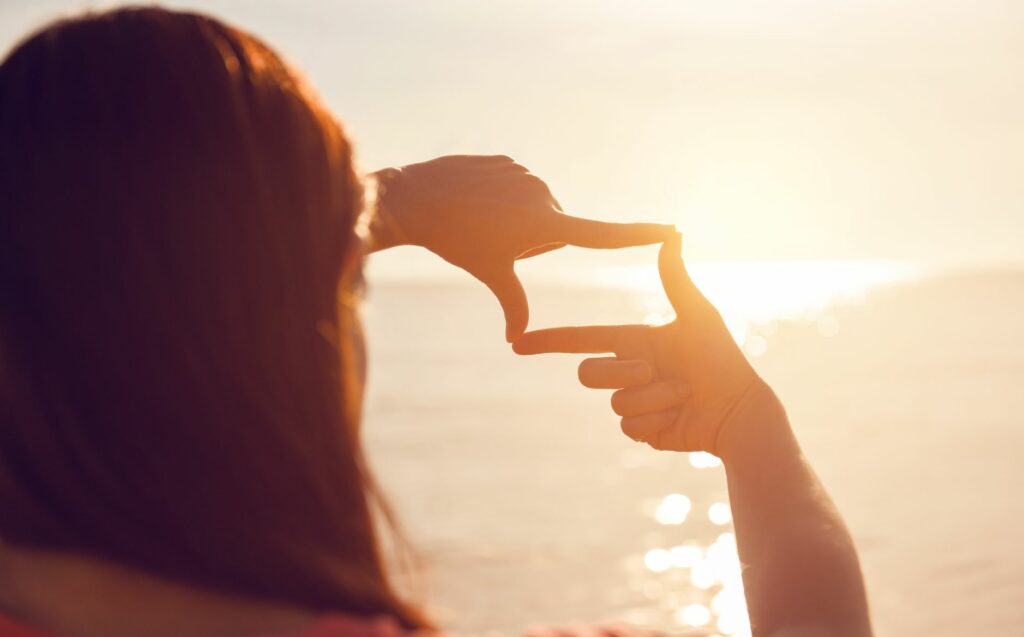 Frau mit Händen zu einem Ausschnitt auf den Horizont bei Sonnenuntergang