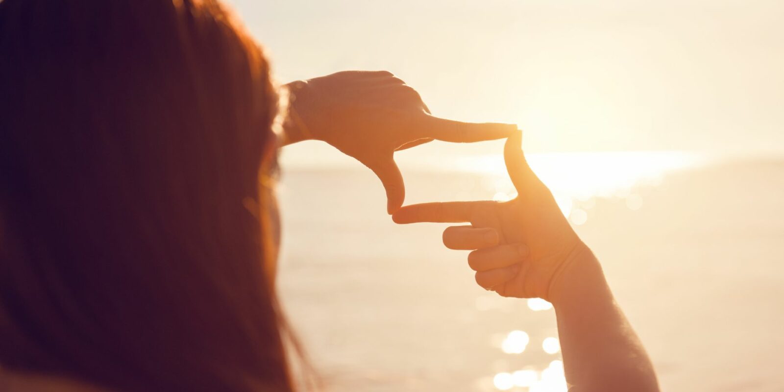 Frau mit Händen zu einem Ausschnitt auf den Horizont bei Sonnenuntergang