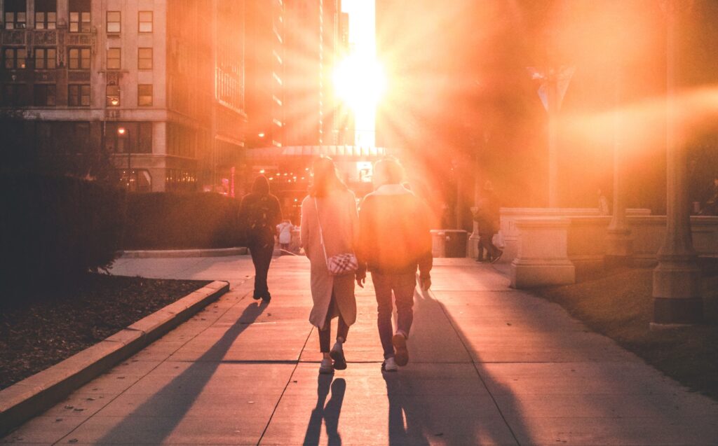 Zwei Menschen laufen zusammen zwischen Häusern Richtung Sonnenuntergang