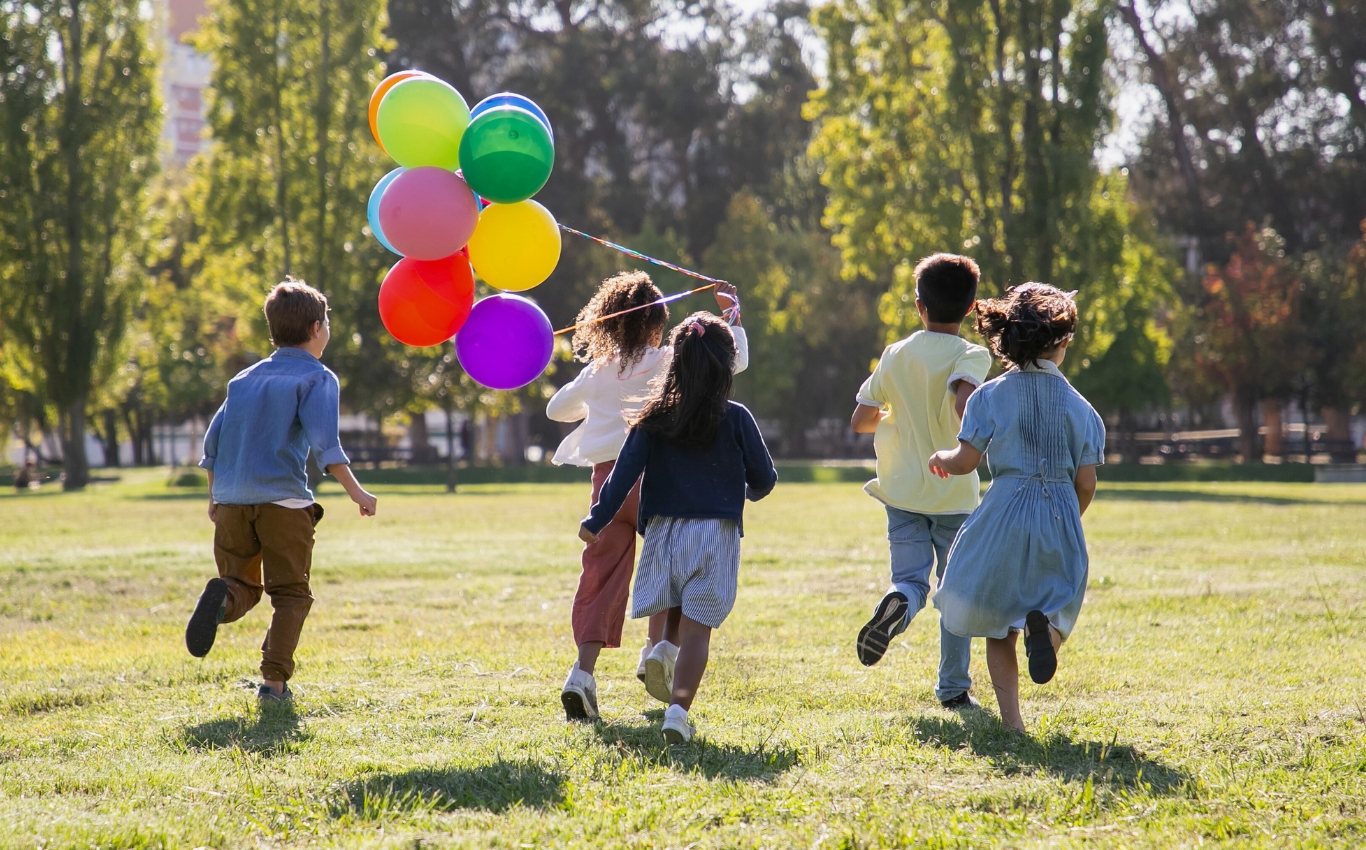 Kinder rennen auf Wiese mit bunten Ballons