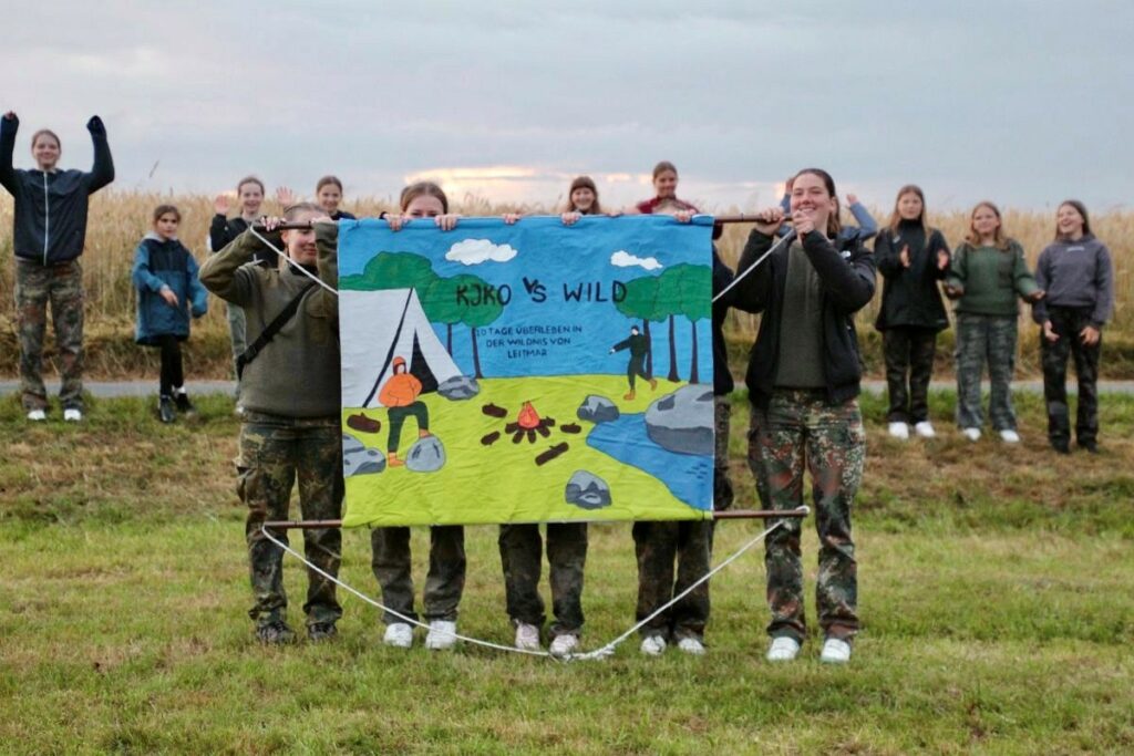Gruppe im Zeltlager mit Banner "KJKO (Katholische Jugend Kloster Oesede)
