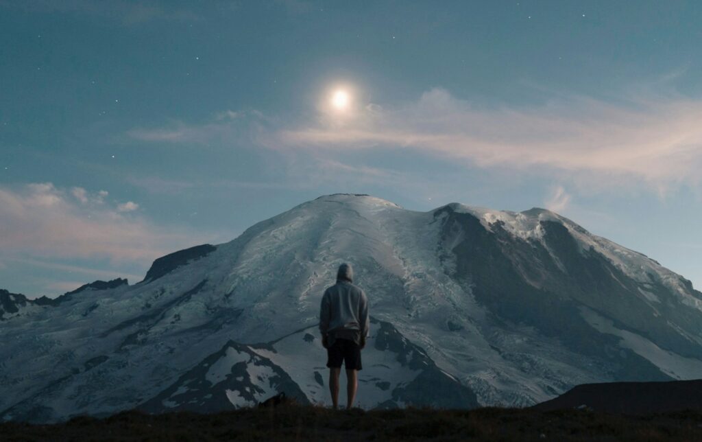 man standing on grass field overlooking mountain