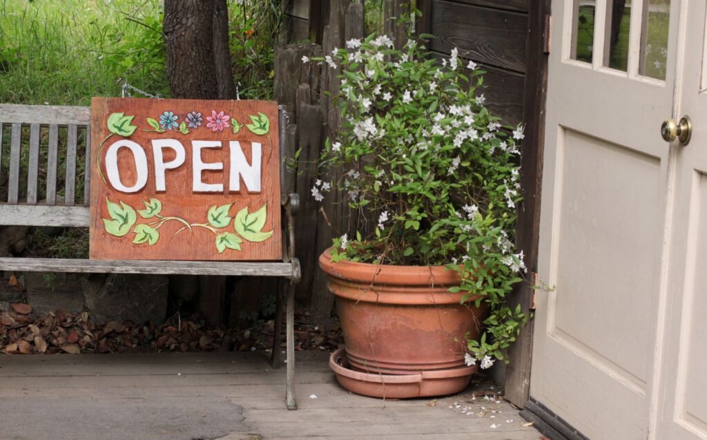 "Open" Schild mit Blumen vor Tür