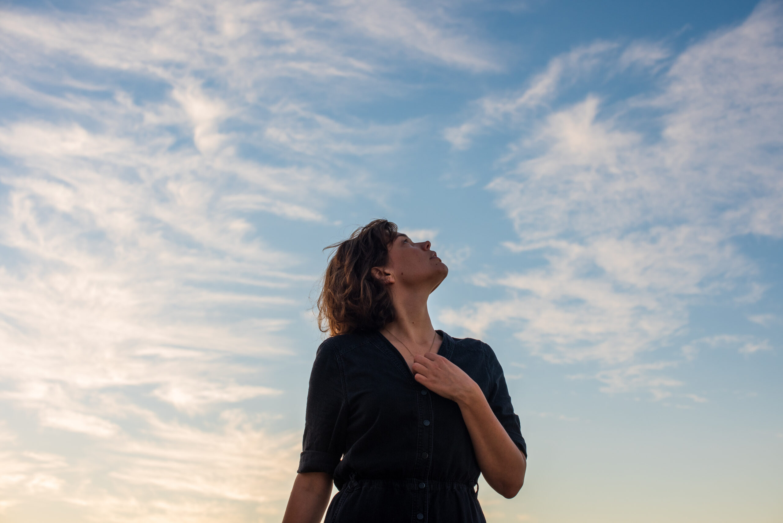 Frau blickt in den Himmel mit Hand aufs Herz.