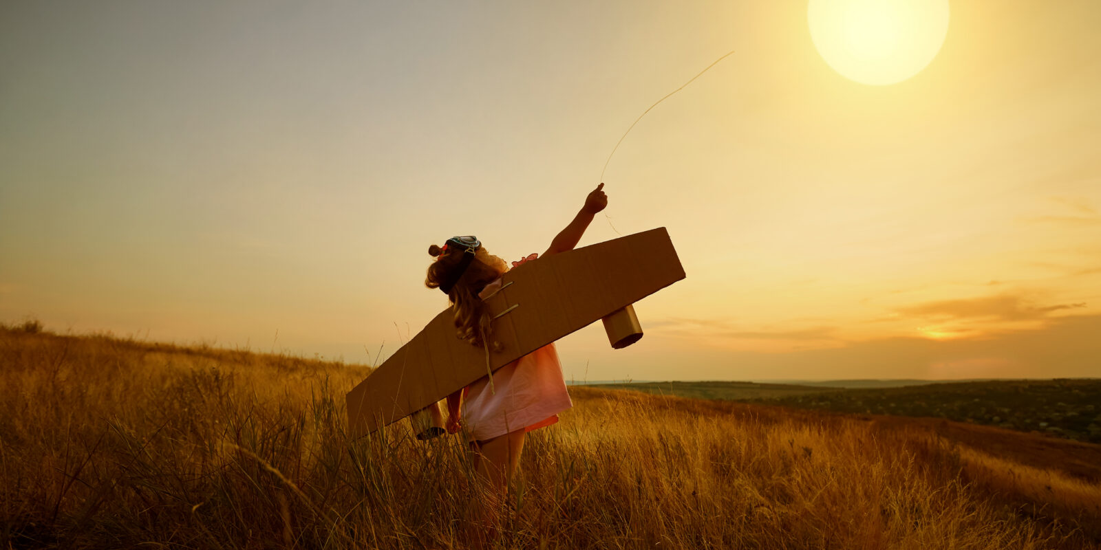 Kind, dass auf einem Feld im Sonnenuntergang Flugzeug spielt