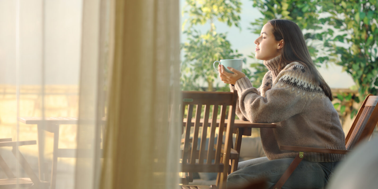 Frau sitzt vor dem Fenster mit einer Tasse Kaffee